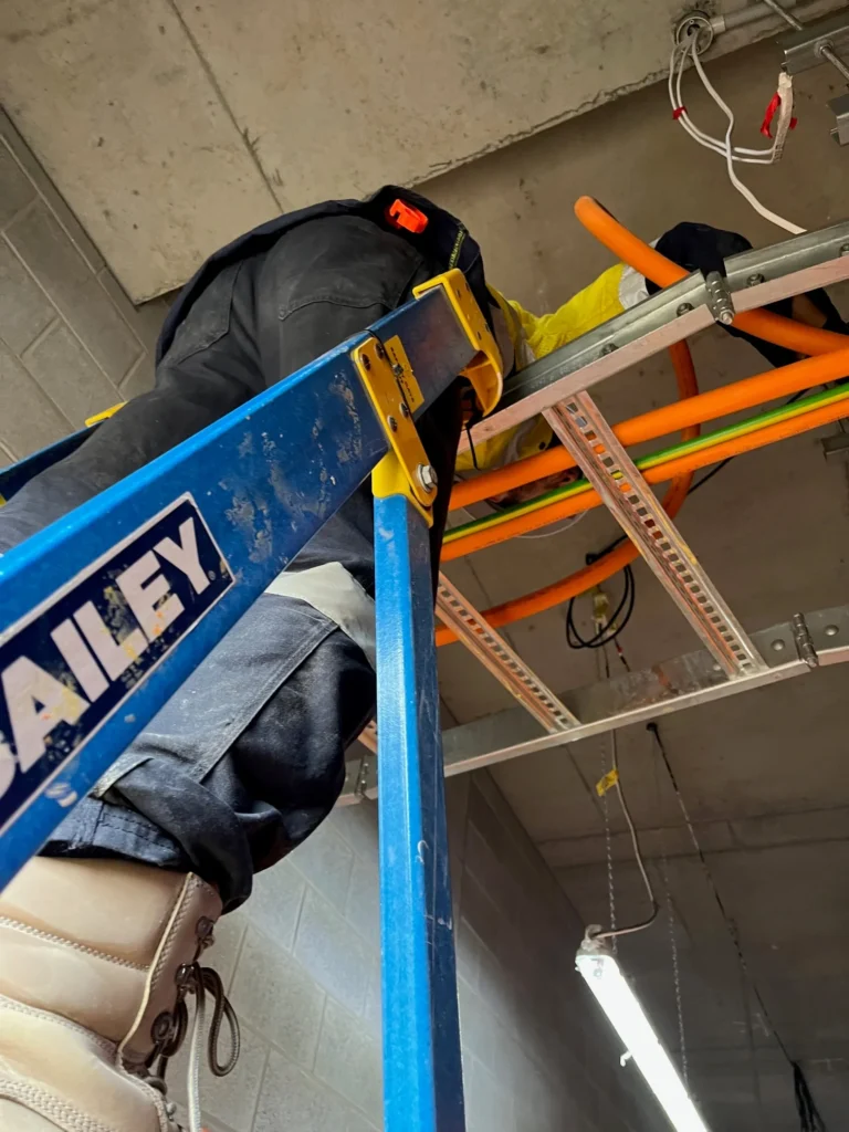 Electrician on a ladder working on overhead hospital cable routes
