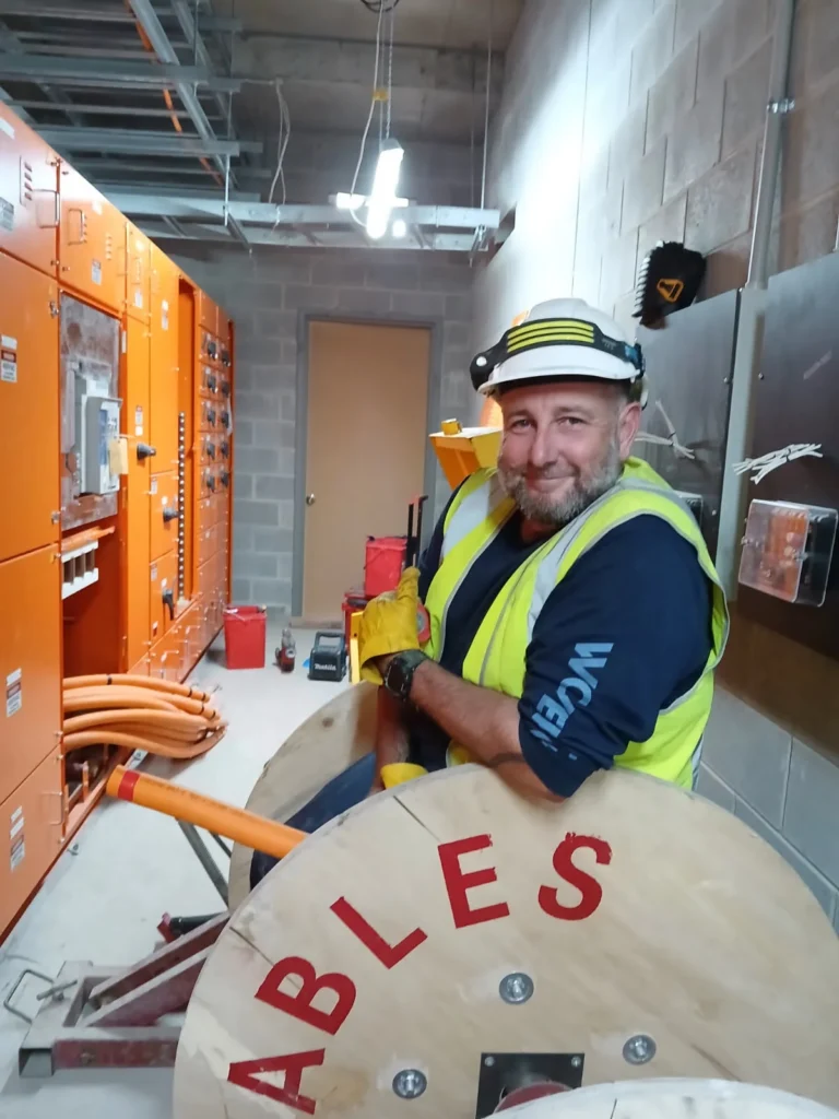 Electrician handling a cable drum beside hospital switchboards